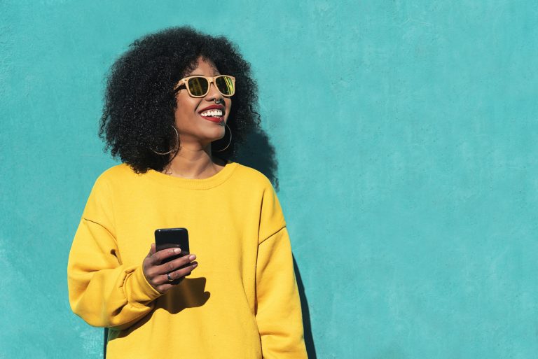 Young woman in sunglasses against a blue wall using a smartphone