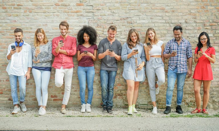 Group of young people standing against a wall using their smartphones