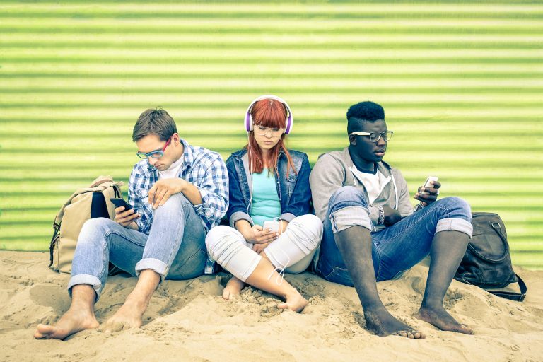 2 men and 1 woman on their phones at the beach