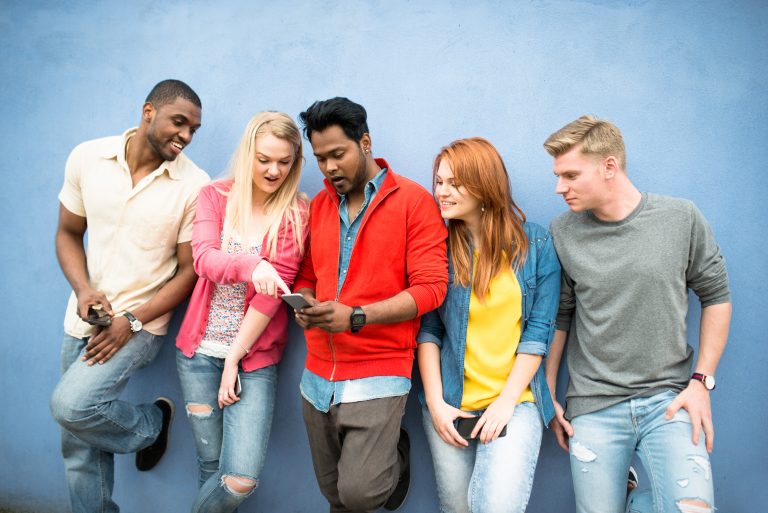 Group of young people gathered at a wall looking at their friend's phone