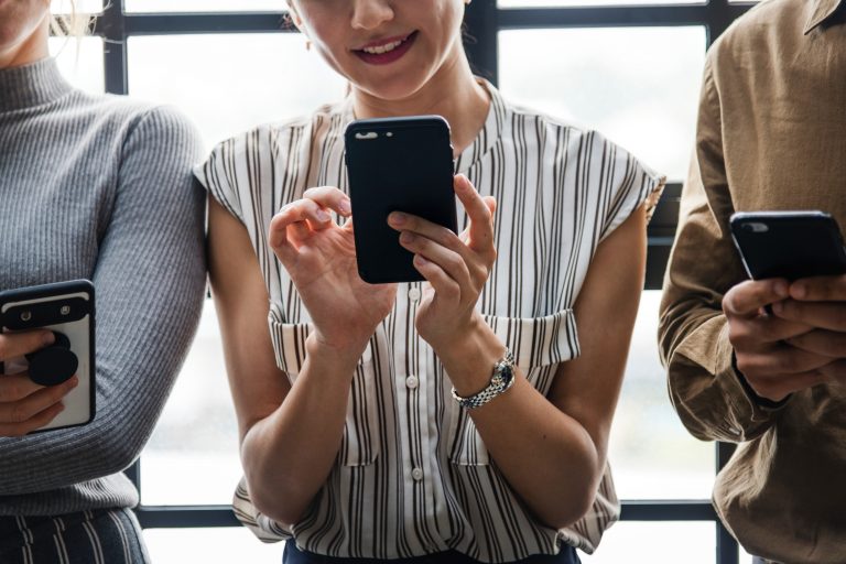 Close-up of three people against a window using their smartphones